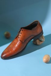 Studio shot of a stylish brown leather men's shoe on a blue backdrop with nuts.